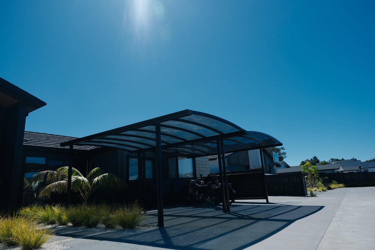 A custom carport with a grey polycarbonate roof and a black frame, made by GC Living Auckland. 